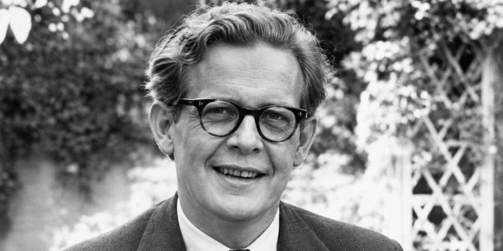 Black-and-white vintage portrait of a young Jean Piaget wearing glasses and a suit, smiling outdoors.